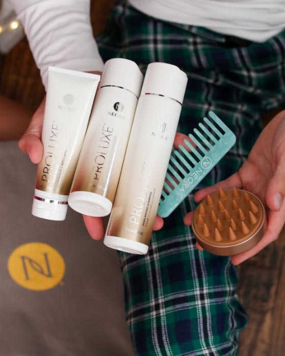 Man holding Neora's hottest holiday must-have, the Get-Gorgeous Holiday Hair Set, which includes ProLuxe™ Rebalancing Shampoo, ProLuxe™ Rebalancing Conditioner, ProLuxe™ Hair Mask, FREE Detangling Comb + FREE Scalp Scrubber and FREE Gift Bag.  